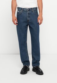 Jean en denim bleu avec une coupe droite, cinq poches et une fermeture à bouton. Tissu texturé avec des détails de décoloration subtils.