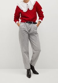 Roter gestrickter Pullover mit einem weißen Spitzenkragen, kombiniert mit hochgeschnittenen grauen Jeans und spitzen schwarzen Knöchelstiefeln.