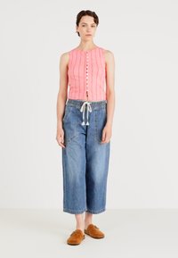 Gaiši rozā cropped tops ar ribinātu tekstūru un pogām, kas apvienots ar ziliem plaša kāju džinsiem ar vilkšanas jostu un sānu kabatām.