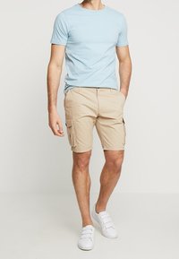 Světle modré tričko s krátkým rukávem v kombinaci s béžovými cargo šortkami se bočními kapsami. Bílé tenisky dotvářejí celý outfit.