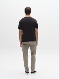 Must lühikeste varrukatega t-särk, helebeež õhuke pükste istuvusega ja mustad tossud, nähtavad tagant valgel taustal.