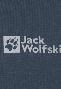 Tessuto blu navy con una superficie liscia presenta un logo con una impronta di zampa bianca e il testo "Jack Wolfskin" in un carattere sans-serif in grassetto.