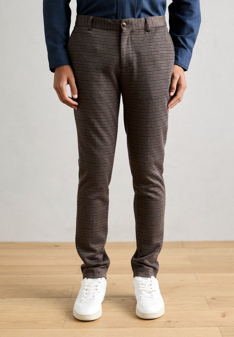 Brown patterned trousers featuring a slim fit, textured fabric, belt loops, and a front button closure, paired with white sneakers.