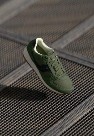 Green athletic shoe featuring a mix of suede and mesh materials, textured surface, white midsole, and brown rubber outsole.