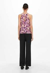 Top sin mangas con estampado floral en tonos de rosa y púrpura, que presenta un diseño de espalda con forma de ojales, combinado con pantalones anchos negros.