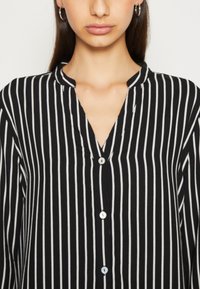 Black and white striped shirt with a notch collar, featuring a button-down front and smooth fabric texture.