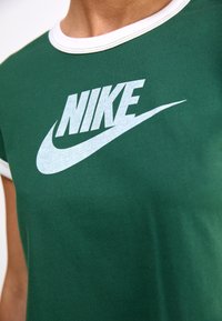 Grön bomullströja med vit rund halsringning och en oversized Nike-logotyp i ljusgrått, med en mjuk textur och avslappnad passform.