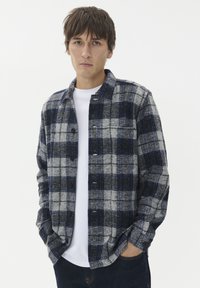 Flanelasta srajca z vzorcem v sivo, mornarsko modri in modri barvi, z gumbom na sprednji strani, dolgimi rokavi in žepom na prsih.