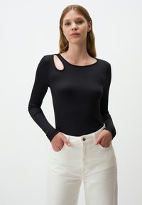 Bodysuit nero a maniche lunghe con texture a costine, caratterizzato da un design unico con taglio sulle spalle, abbinato a jeans bianchi a vita alta.