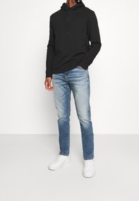 Felpa con cappuccio nera in cotone, vestibilità comoda, abbinata a jeans in denim azzurro chiaro con una lavaggio sfumato. Sneakers bianche completano l'outfit.