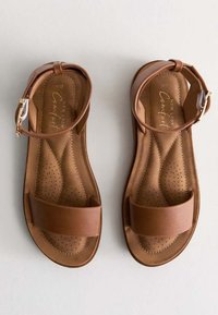 Sandali in pelle marrone con design piatto, dotati di ampie cinghie per le dita, cinghie alla caviglia regolabili e plantari perforati per la traspirabilità.