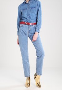 Jeansskjorta med två bröstfickor, tillsammans med ljusblå jeans och ett rött bälte. Guldiga spetsiga ankelskor fulländar outfiten.