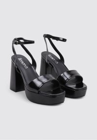 Sandalias de plataforma negras con tira ancha en los dedos y correa en el tobillo. Fabricadas en material brillante, cuentan con un tacón alto chunky y una plantilla acolchada.