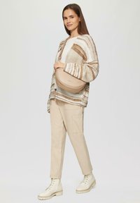 Beige leren schoudertas met een halfcirkelvorm, gladde textuur en subtiel logo. Gdragend met een gestreepte gebreide cardigan en crèmekleurige broek.