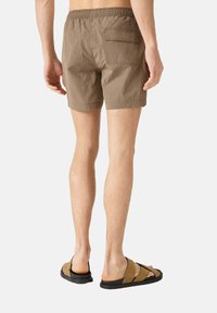 Bruine, gestructureerde zwembroek met een elastische tailleband en een achterzak, gecombineerd met bruine slippers.