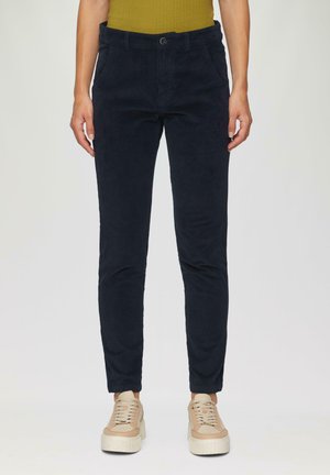 Pantalons en velours côtelé bleu marine avec une coupe slim, dotés de poches avant et d'une fermeture à bouton, associés à des baskets beiges.