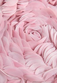 Vrstvené ružové látkové lupene usporiadané do hustého, víriaceho ružového vzoru s jemnou textúrou a priehľadnými okrajmi.