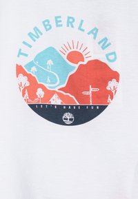 Witte t-shirt met een circulaire graphic in blauwe, rode en zwarte kleuren. De tekst luidt "TIMBERLAND" en "Laten we plezier hebben." Inclusief natuurmotieven.