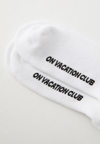 Valged puuvillased sokid, millel on must tekst "ON VACATION CLUB" tikandina igal sokil. Pehme tekstuur klassikalise meeskonna disainiga.