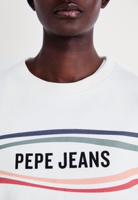 Sudadera blanca con un estampado gráfico que presenta el texto en negrita "PEPE JEANS", acentuado por rayas curvas en verde, rosa y azul marino. Cuello de barco.