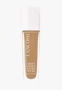 Foundationflaske med en klar glassbunn, beige væske inni, og et høyt hvitt lokk. Har etiketter med "Lancôme" og "Teint Idole Ultra Wear".
