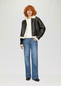 Veste en cuir noir avec col et poignets en shearling crème, associée à un jean léger évasé bleu clair et des chaussures noires. Design simple et moderne.