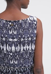 Námořnické a bílé vzorované bezrukávové šaty s kulatým výstřihem a nastavitelným knoflíkem na zadní straně, s jemnou texturou látky.