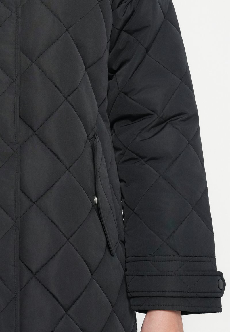 Gequilted zwarte jas met een diagonale patroon, een zijzak met flap en knoopsluiting bij de mouwen. Zachte textuur en mouwen van middellange lengte.