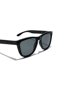 Mustad plastist päikeseprillid, matt viimistlusega, ristkülikukujuliste läätsedega ja halli tooniga. Pudelisangadel on brändinimi "HAWKERS".