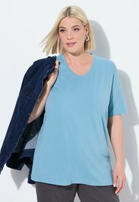 T-shirt azzurro a maniche corte realizzato in morbido tessuto, con scollatura rotonda e vestibilità rilassata. Il modello tiene una giacca di jean.