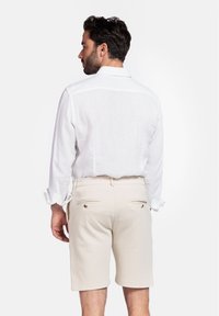 Lichtgewicht witte linnen blouse met opgerolde manchetten, gecombineerd met beige shorts met achterzakken en decoratieve knopen.