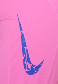 Feszes rózsaszín sportfelső kék Nike logo-val, mely mintás dizájnnal rendelkezik, kiemelkedően sima, rugalmas anyagból és precíz varrásokkal.