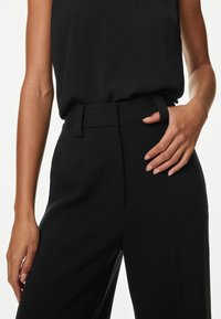 Zwarte tailorpantalons met een hoge taille, met een gladde textuur, riemlussen en zijzakken. Gekleed met een bijpassende top.
