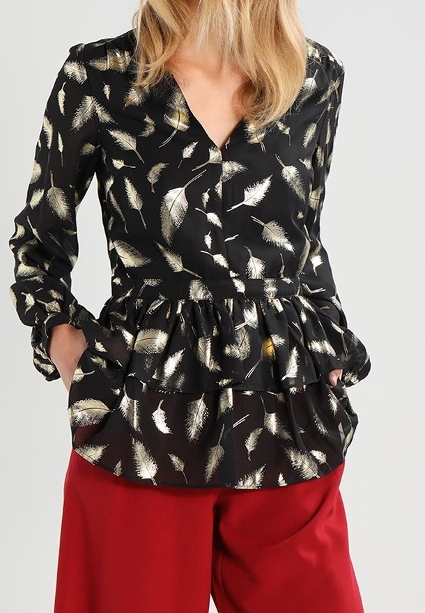 Blusa nera con motivo di piume oro e bianco, vita peplum, chiusura con bottoni, maniche lunghe raccolte ai polsi, abbinata a pantaloni larghi rossi.