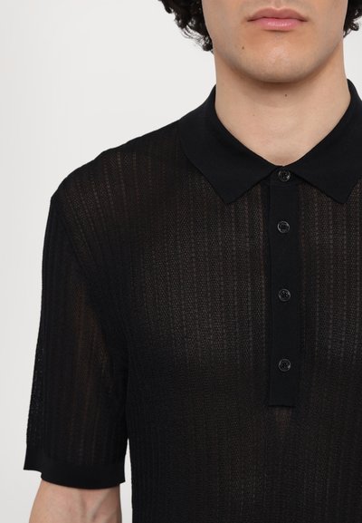 Fekete, rövid ujjú pólóing, áttetsző, textúrált anyagból, bordázott mintázattal, klasszikus gallérral és hat fekete gombbal az elején.