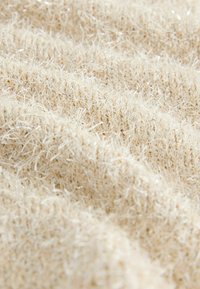 Beige strukturiertes Gewebe mit flauschigen Fasern und subtilen metallischen Fäden, das eine weiche, plüschige Oberfläche schafft, ideal für Textilien wie Decken oder Bekleidung.