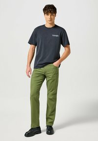 Zwarte katoenen t-shirt met wit "Wrangler" logo, gecombineerd met olijfgroene broek en zwarte veterschoenen. Eenvoudig ontwerp, casual pasvorm.