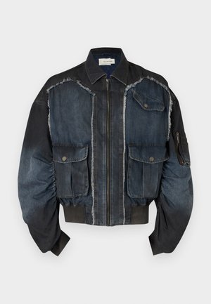 Άνδρας που φοράει μαύρο και σκούρο μπλε μπουφάν με φερμουάρ και μεγάλες τσέπες, σκούρα μπλε βερμούδα μέχρι το γόνατο, λευκές κάλτσες και μαύρα επίσημα παπούτσια.