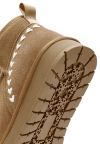 Stivaletto alla caviglia in suede beige con cuciture a forma di cuore bianche. La suola in gomma presenta un motivo a fiocco di neve per garantire una buona aderenza.