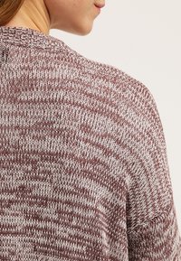 Maglione a maglia in bordeaux e bianco, caratterizzato da un motivo testurizzato. I dettagli includono un ampio scollo e una vestibilità ampia, che mettono in mostra un tessuto morbido e a coste.