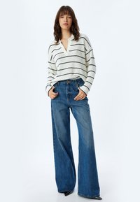 Maglione a righe bianche e nere con scollatura a V, abbinato a jeans blu a vita alta e gamba ampia. Tessuto morbido; vestibilità comoda; stile casual.