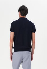 Mørkeblå kortermet polo med krage, tettsittende design og ribbet kant. Kombinert med lysegrå bukser med to baklommer.