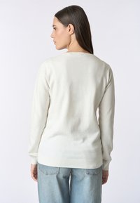 Maglione beige chiaro con maniche lunghe, polsini e orlo a costine, texture morbida e collo tondo classico, abbinato a jeans blu chiaro.