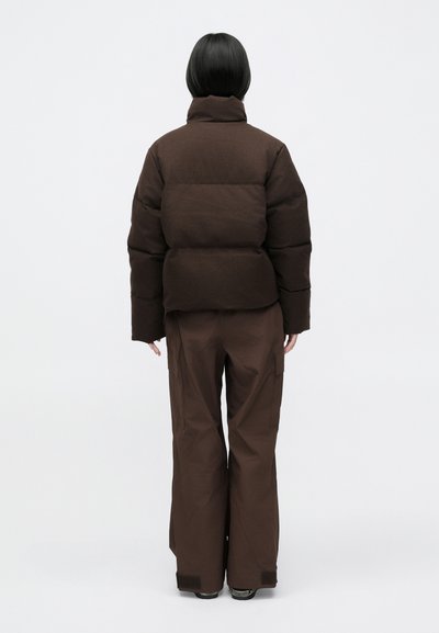 Doudoune marron avec un col montant et une coupe boxy, associée à un pantalon marron ample avec des poches cargo et une texture lisse.