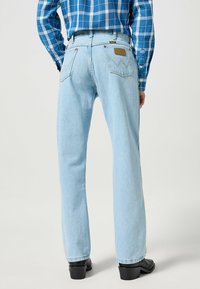 Jean en denim bleu clair avec une coupe droite, présentant une patch en cuir à l'arrière et deux poches arrière avec une couture distinctive.