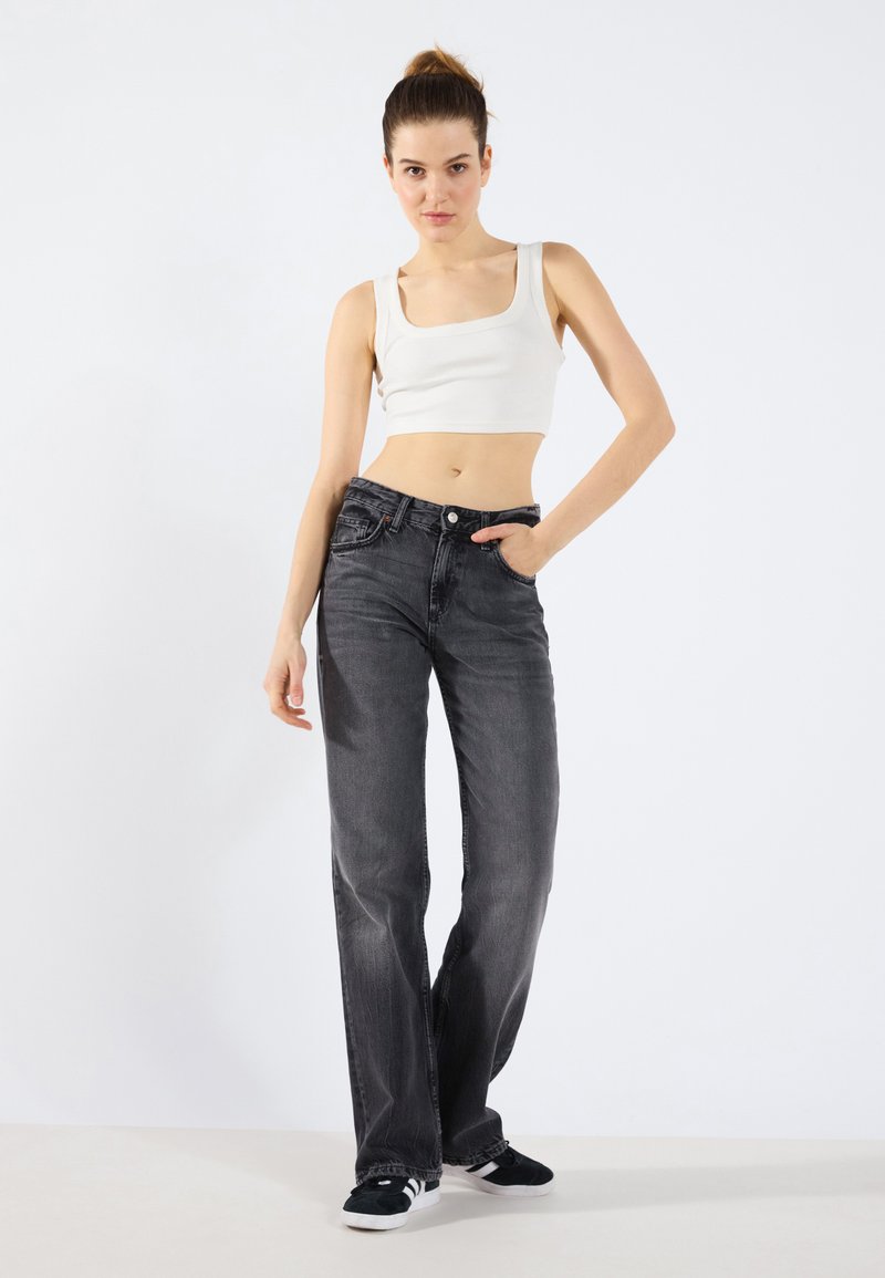 Jeans negre cu croi drept și un finisaj decolorat, asortate cu un crop top alb mulat. Look-ul este completat cu adidași negri.