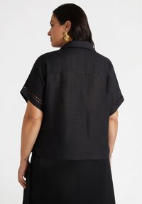 Camicia nera in lino a maniche corte con colletto, decorata con ricami sulle maniche e dal fit rilassato, abbinata a una gonna nera plissettata.