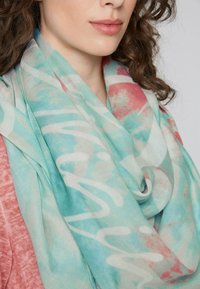 Woman wearing a pink top and a loosely wrapped pastel scarf with blue, white, and coral abstract patterns around her neck.