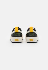 Sapatos Vans com parte superior em preto e branco, com detalhes em amarelo no calcanhar, tecido texturizado e sola de borracha. Logotipo exibido no calcanhar.