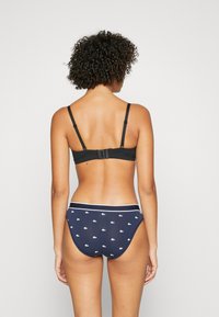 Melna krūšturis ar regulējamiem siksniņām un āķa aizdari, kopā ar tumši ziliem apakšbiksēm ar mazu baltu logotipa rakstu un kontrastējošu jostas daļu.